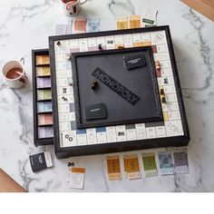 a monopoly board game on a marble table next to coffee mugs and other items