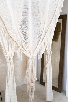 a white bed with tassels hanging from it's sides and two mirrors in the background