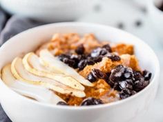 a bowl filled with cereal and blueberries on top of a white table cloth next to a cup of coffee