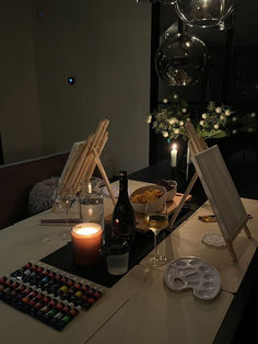 the table is set up for an art party with candles, wine glasses and paintings