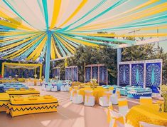 an outdoor wedding venue with yellow and blue decorations on the ceiling, tables set up for guests