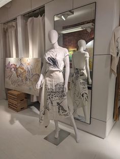 mannequins in front of a mirror with clothes on the floor and paintings behind them