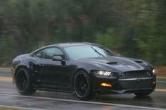 a black sports car driving down the road in the rain with its hood up and lights on