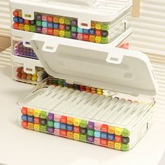 two white boxes filled with colorful crayons sitting on top of a table next to each other