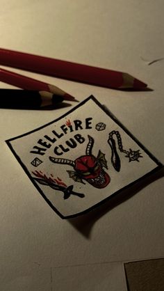 two pencils are laying next to a paper with the words hellfire club on it