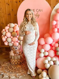 a pregnant woman standing in front of balloons and decorations for her baby's first birthday