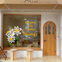 a store front with flowers in the window and an empty bench behind it that says enjoy the little things