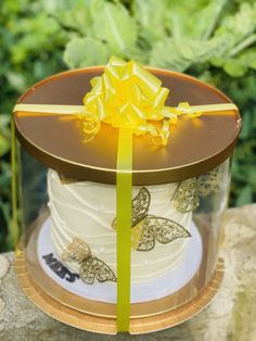 there is a cake that has been decorated with yellow ribbon and bow on top, sitting in front of some bushes