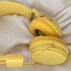 a pair of yellow headphones laying on top of a white bed sheet and pillow