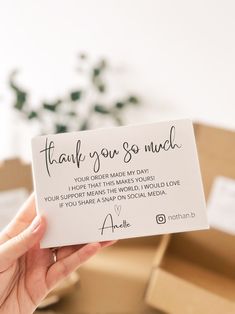 a person holding up a thank you so much card in front of boxes with flowers