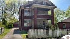 an old brick house with a white picket fence in front of it and two cars parked on the street