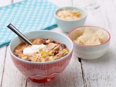 two bowls of mexican chicken soup with sour cream and tortilla chips on the side