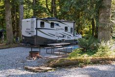 an rv is parked in the woods near picnic tables