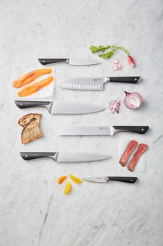 several knives and slices of bread on a marble counter top with garlic, lemons, onion, and pepper