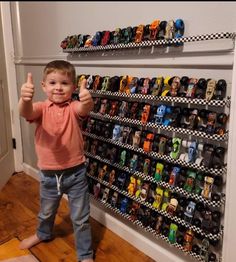 a young boy giving the thumbs up in front of a display of cars and trucks