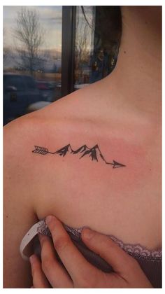 a woman's shoulder with an arrow and mountains tattoo on the left side of her upper arm