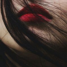 a woman's face with red lipstick on her lips and long black hair in the foreground