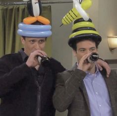 two men with hats on their heads, one holding a camera and the other looking at something