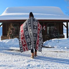 a person walking in the snow with a blanket on their back and a cabin in the background