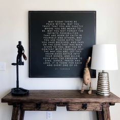 a wooden table topped with a lamp next to a framed poem