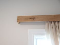 a wooden shelf above a window in a room with white walls and drapes on the windowsill