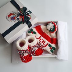 an open box with two knitted hats and mittens in it next to a white gift bag