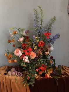 a vase filled with lots of colorful flowers on top of a wooden table next to a wall