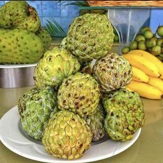 there are many different fruits on the plate and one is green with yellow bananas in the background