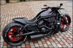 a black and red motorcycle parked on top of a brick floor next to a tree