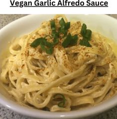 a white bowl filled with pasta and garnished with parsley on the side