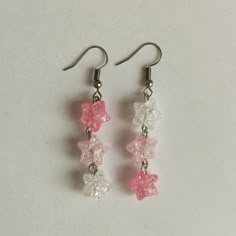 two pink and white flowers are hanging from silver earwires on a white surface