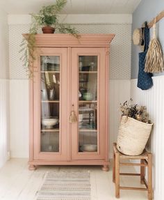 a pink china cabinet sitting in the corner of a room next to a potted plant