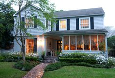 a white house with black shutters on the front and side windows, surrounded by green grass