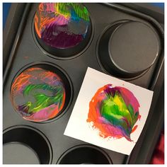 a muffin tin filled with cupcake pans covered in colorful icing next to a piece of paper