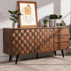 a wooden cabinet with an art piece on top of it next to a potted plant