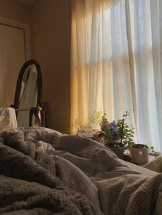 an unmade bed in front of a large window with sheer curtains and flowers on it