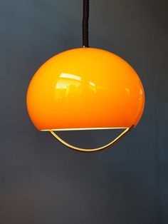 an orange light hanging from a black cord on a gray wall in a dark room