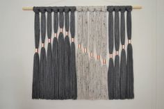 the wall hanging is made out of gray and white yarn with copper pins on it