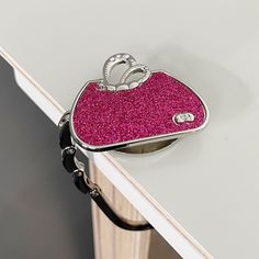 a pink purse sitting on top of a white table next to a black bag with a diamond ring