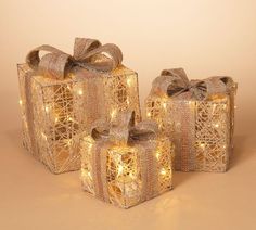 three wrapped gift boxes with bows and fairy lights on the sides, all decorated in gold