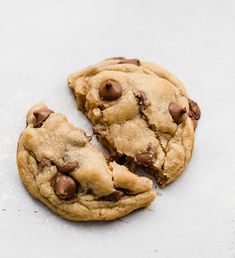 two chocolate chip cookies sitting on top of a white counter next to one cookie broken in half