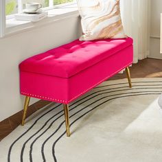 a bright pink bench sits in front of a window with white curtains and a rug on the floor