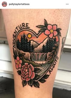 a heart shaped tattoo with flowers and mountains in the background on someone's leg