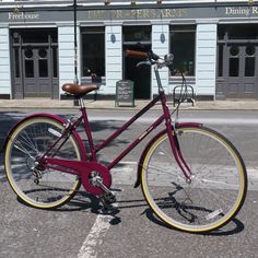 a red bike parked in front of a building on the side of the road with no people around it