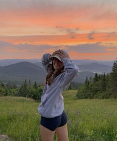 a woman standing on top of a lush green field under a pink and orange sky