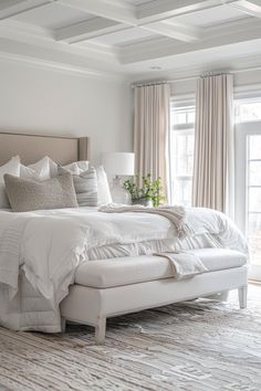 a large white bed sitting in a bedroom next to a window with drapes on it