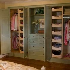 an open closet with clothes hanging on the walls and drawers in front of it, next to a bed