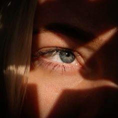 a woman's blue eyes are shown through the shadow of her hand and head