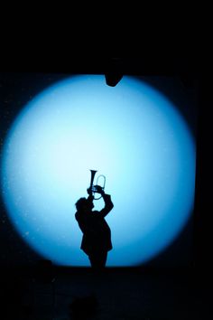 a person holding a trumpet in front of a blue ball with the light shining on it