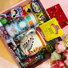 a box filled with lots of different types of snacks and drinks next to some flowers